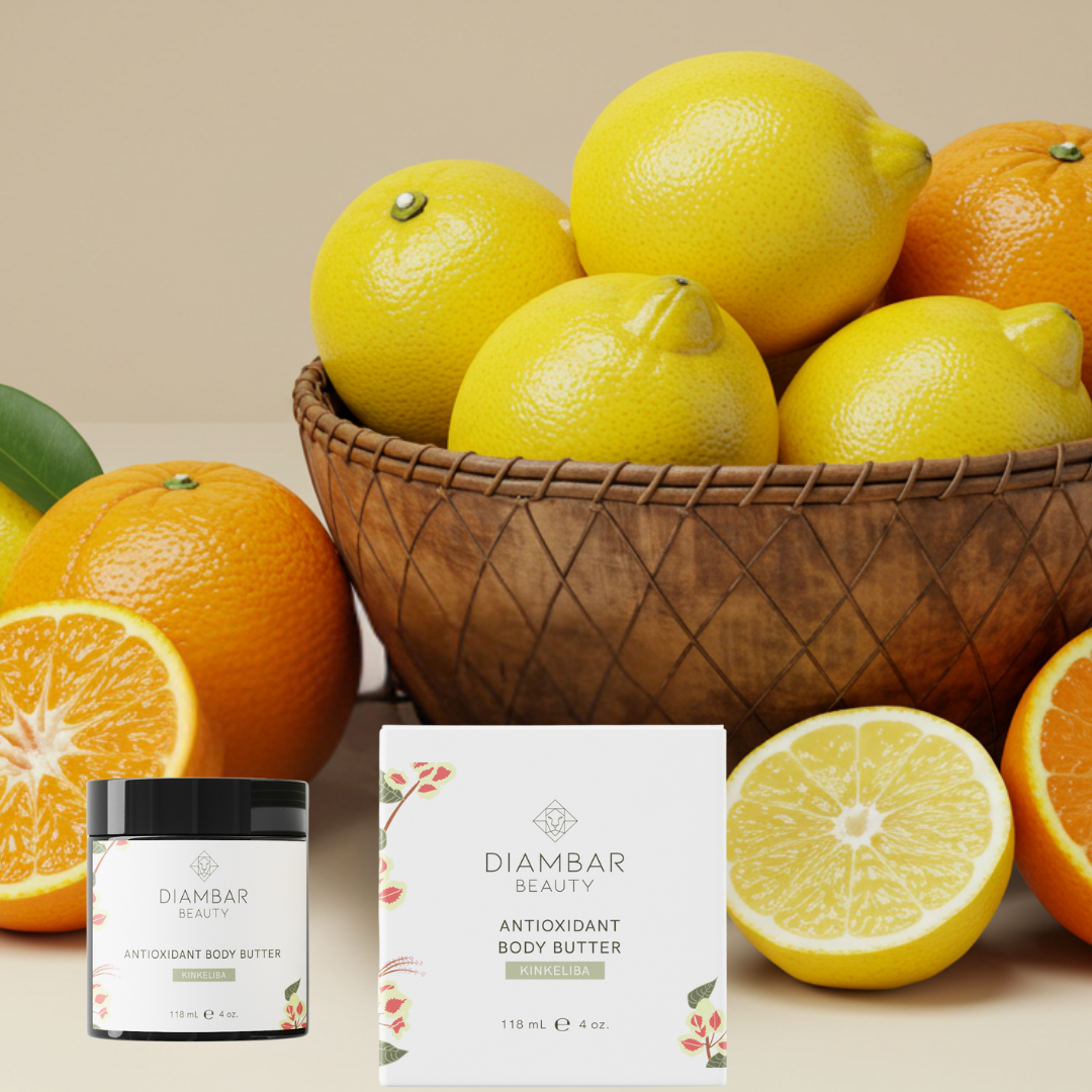 Diambar Beauty's Antioxidant Body Butter in an elegant jar, surrounded by vibrant citrus fruits. A traditional Fulani calabash brimming with fresh lemons and oranges sits in the background, highlighting the butter’s nourishing, antioxidant-rich ingredients.