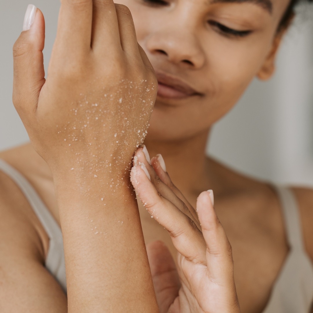 A close-up of the Kinkeliba Smoothing Body Polish texture as a woman gently rubs it onto her hand, revealing its rich exfoliating formula.